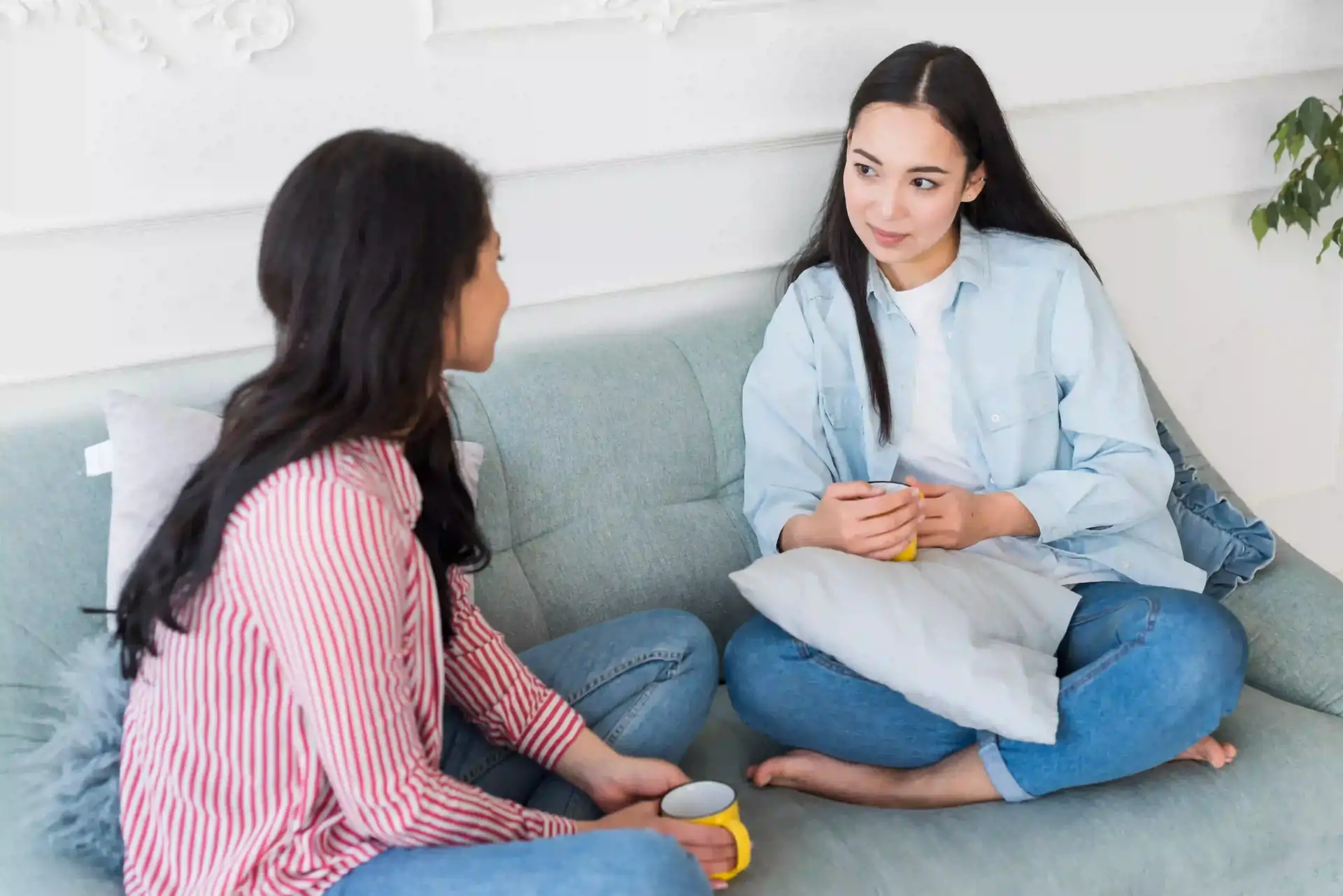 Two women having a relaxed and engaged conversation on a couch, representing the essence of growth - oriented communication that enhances relationships.